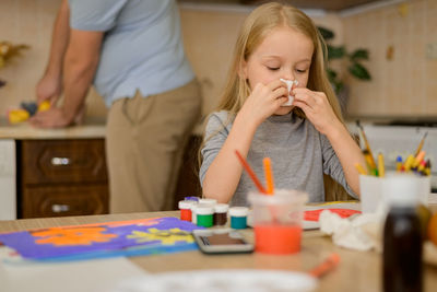 Sick child wipes his nose with a napkin at home, dad prepares a drink with lemon