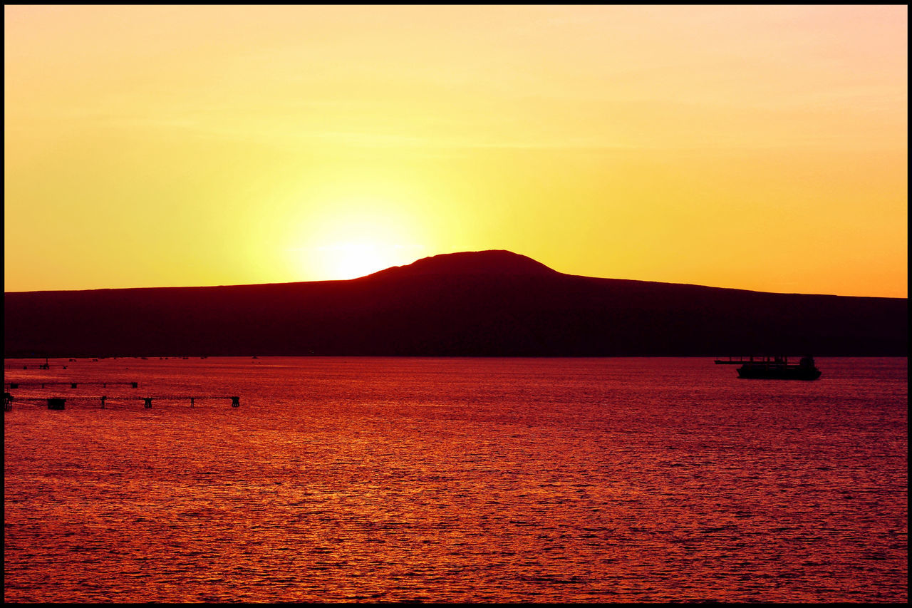 SILHOUETTE MOUNTAIN BY SEA AGAINST ORANGE SKY