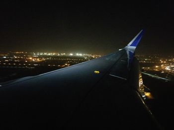 Airplane flying over illuminated city against clear sky at night