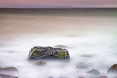 Romantic morning at sea. boulders in smooth sea. pink horizon with first hot sun rays. long exposure