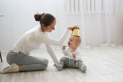 Funny baby 10 months with his mother playing with a pot in the kitchen, lifestyle 