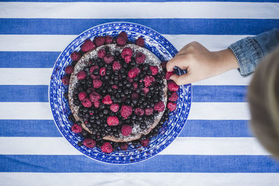Directly above shot of boy picking up raspberry in tart at table