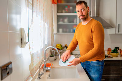 Portrait of man cleaning dish in kitchen at home