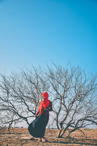 Woman in hijab standing by bare tree on land