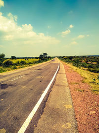 Empty road amidst field against sky