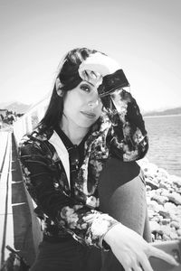 Portrait of young woman sitting by sea against sky