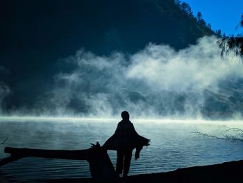Rear view of silhouette woman looking at waterfall against sky