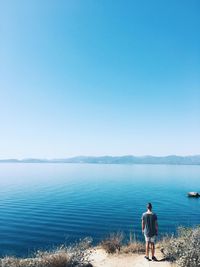 Rear view of man standing at sea against clear sky