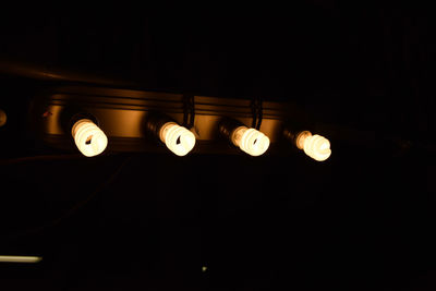 Low angle view of illuminated light bulb hanging against black background