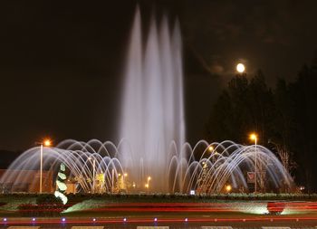 Illuminated light trails on fountain against sky at night