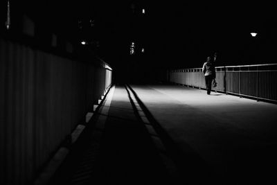 Rear view of woman walking on illuminated bridge at night