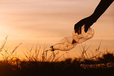 Person hand on field against sky during sunset