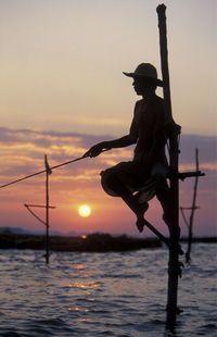 Silhouette fishermen fishing over sea against sky during sunset