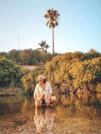 Man sitting by lake against sky