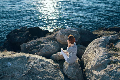 Full length of man sitting on rock at sea shore