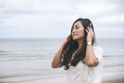  woman listening to music with headphones while standing on shore at beach against sky