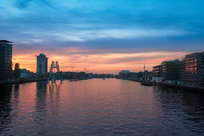 Scenic view of river by buildings against sky during sunset