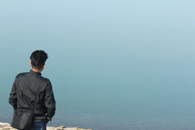 Rear view of young man standing on lakeshore