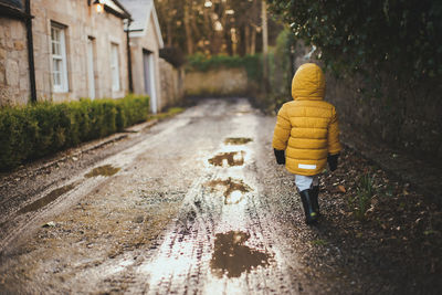 Rear view of boy in yellow coat on small road