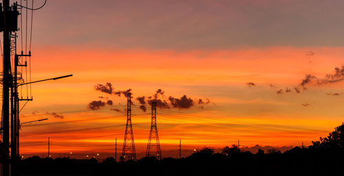 Silhouette trees and electricity pylon against romantic sky at sunset