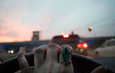 Cropped hand of woman driving car during sunset