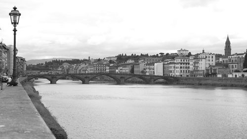 Bridge over river by buildings in city against sky