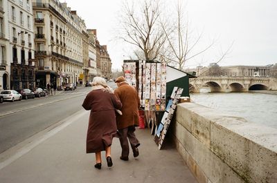 Rear view of senior man and woman walking on street amidst canal and building