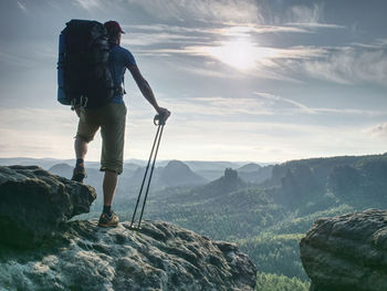 Guy hold sticks in one hand. hiker stop for watching landscape from sharp sandstone summit.