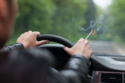 Rear view of mature man holding cigarette while traveling in car