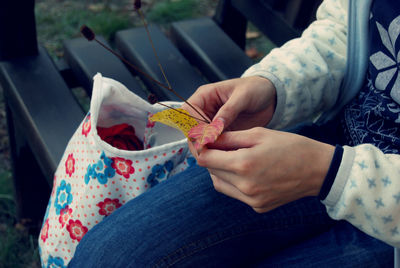 Midsection of woman holding leaves while sitting on bench