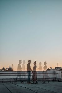 People standing on pier against clear sky during sunset