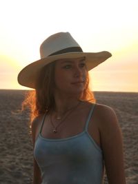 Beautiful woman standing at beach against sky during sunset