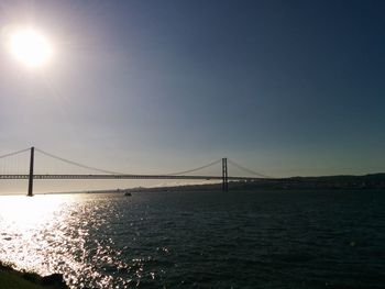 Suspension bridge over sea against clear sky during sunset