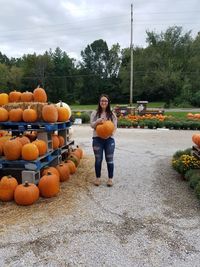 Portrait of young woman holding pumpkin while standing on walkway