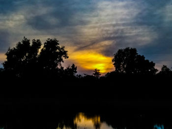 Silhouette trees by lake against sky during sunset