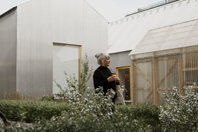 Senior woman with cup of coffee standing in courtyard