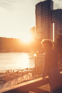 Portrait of woman leaning against railing while standing in city during sunset