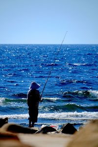 Man fishing in sea against clear sky