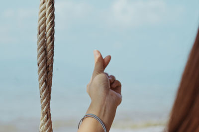 Close-up of hand holding rope against sea