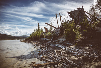 Wooden shipwreck on riverbank against sky