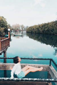 Woman sitting by lake against sky