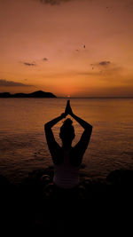 Rear view of woman standing at beach against sky during sunset