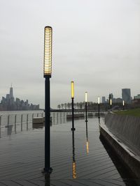 Wooden post on pier by river against sky in city