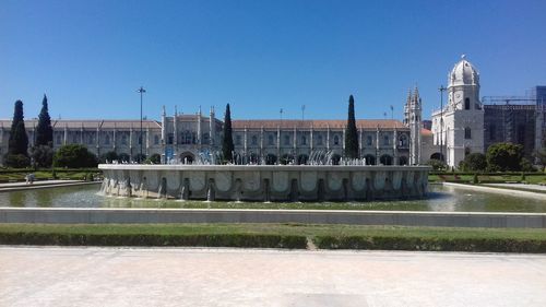 Fountain in city against clear blue sky