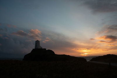 Silhouette rocks on land against sky during sunset