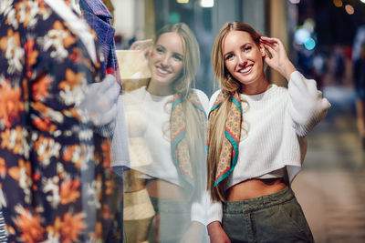 Portrait of smiling young woman standing by glass with reflection