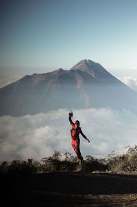 Man with arms raised on mountain against sky