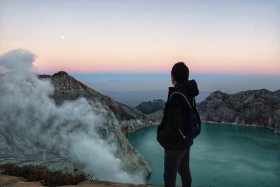 Rear view of man standing on mountain against sky during sunset