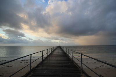 Pier leading towards sea against sky during sunset