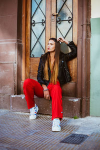 Full length of young woman looking away while sitting at entrance